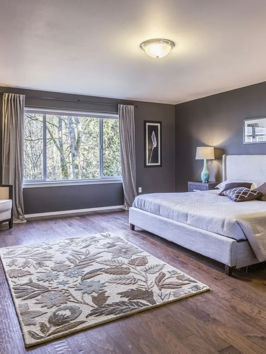 A bedroom with an upholstered bed, bedside lamps and a floral area rug on a dark wooden floor