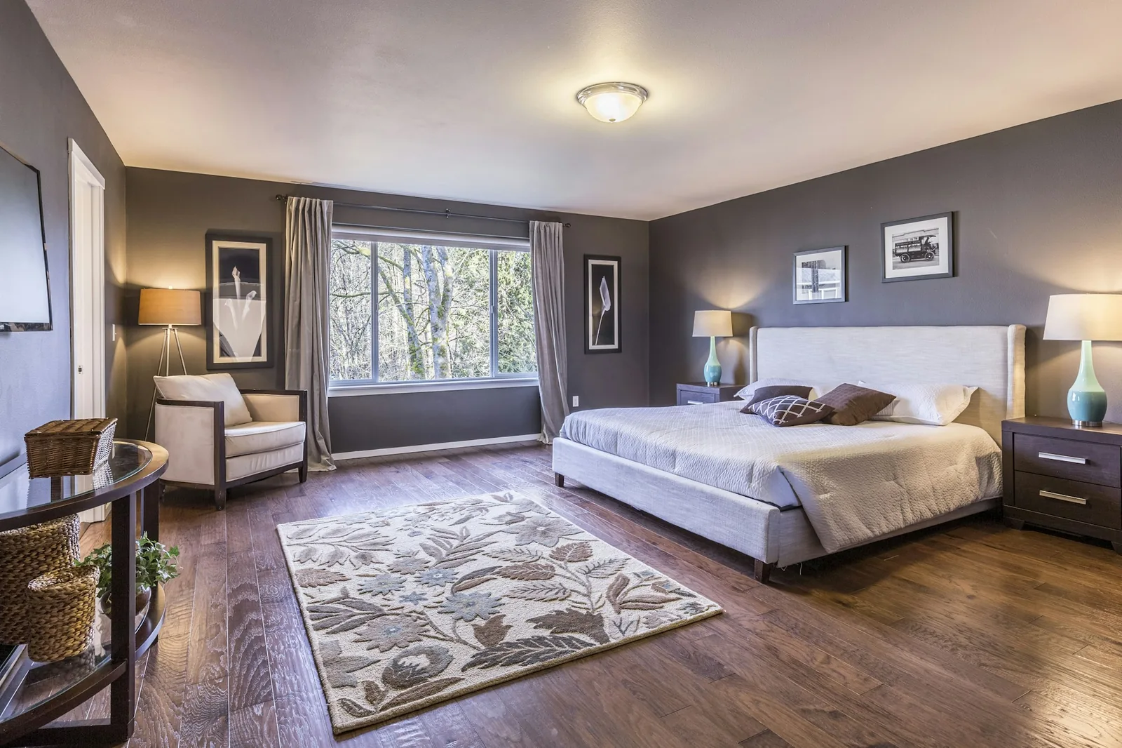 A bedroom with an upholstered bed, bedside lamps and a floral area rug on a dark wooden floor