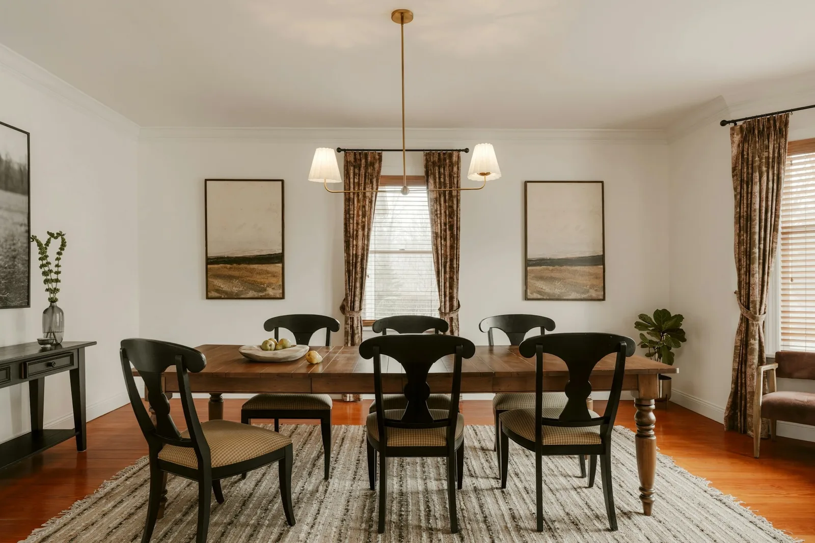A wooden dining table and six black chairs sitting fully on a large striped rug under a pendant light