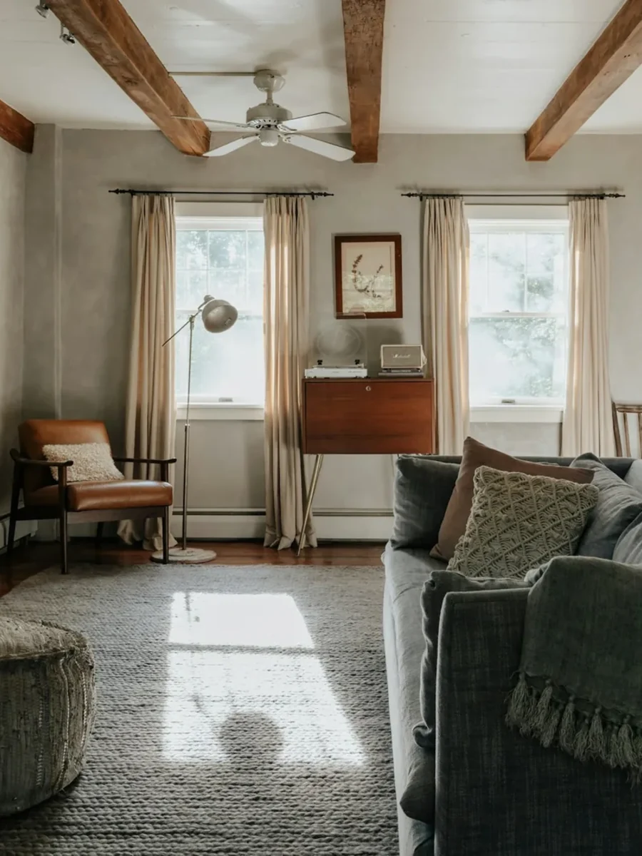 Rustic living room with exposed timber beams, stone fireplace, linen curtains and a grey sofa