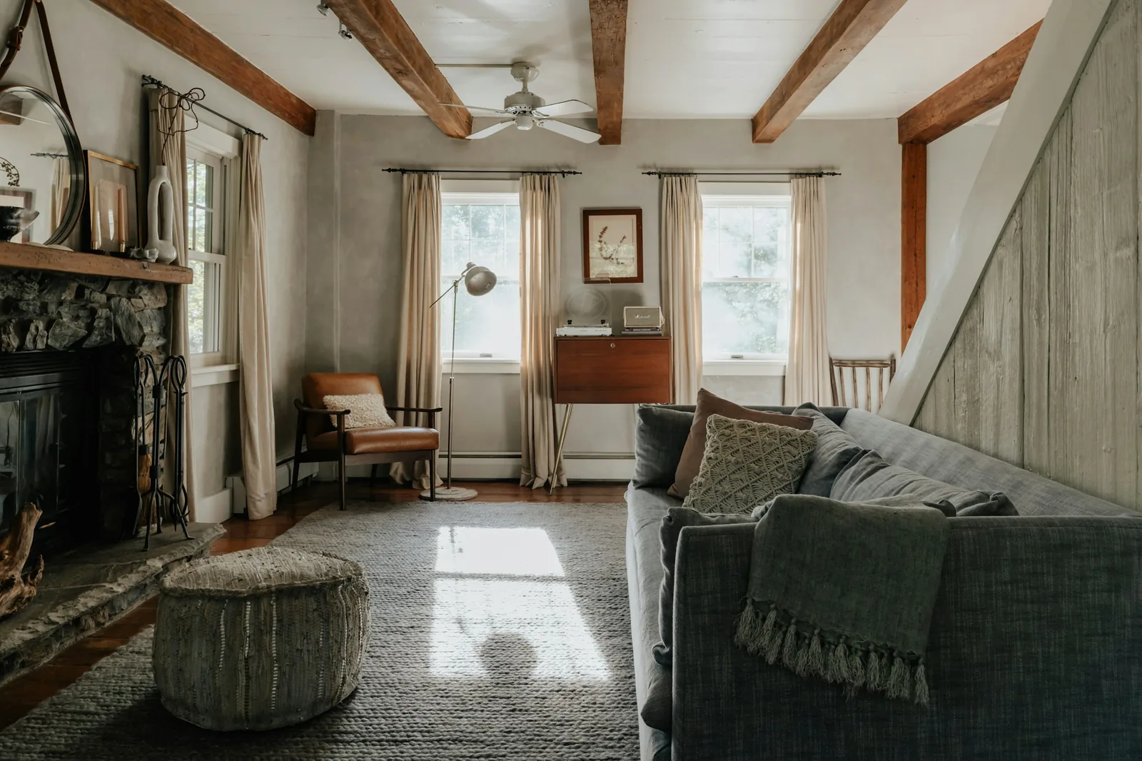 Rustic living room with exposed timber beams, stone fireplace, linen curtains and a grey sofa