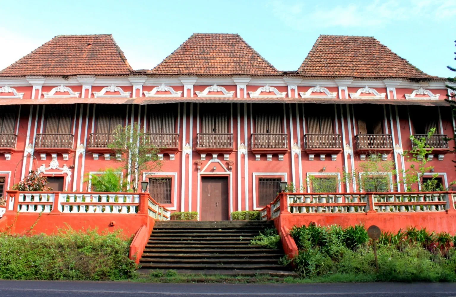 A red-and-white Goan-Portuguese mansion in Margao with three pyramidal gables, balconies and a broad front stair