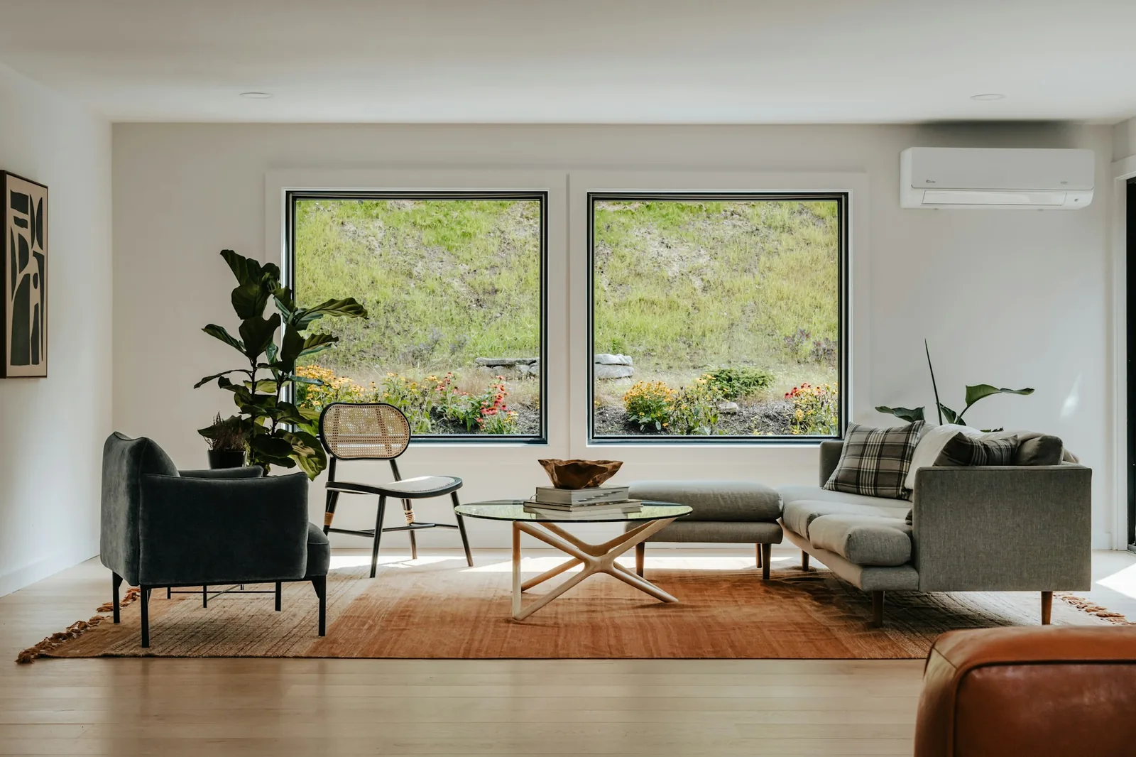 Simple bright living room with a grey sofa, armchair and rug before two large windows