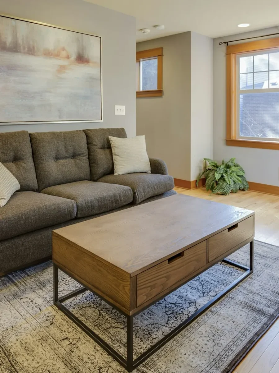 A compact living room with a grey tufted sofa, wooden coffee table and patterned rug in daylight