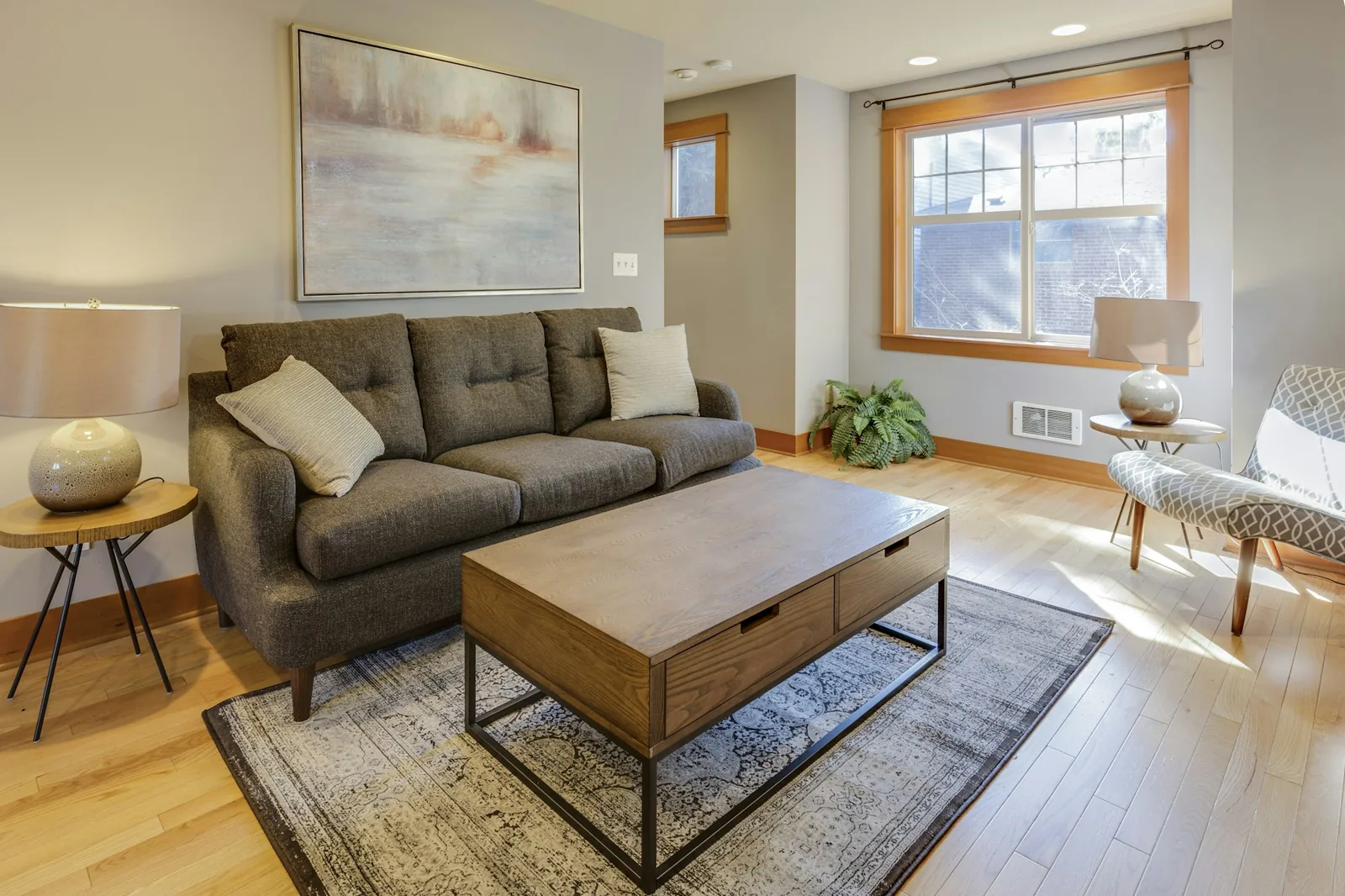 A compact living room with a grey tufted sofa, wooden coffee table and patterned rug in daylight