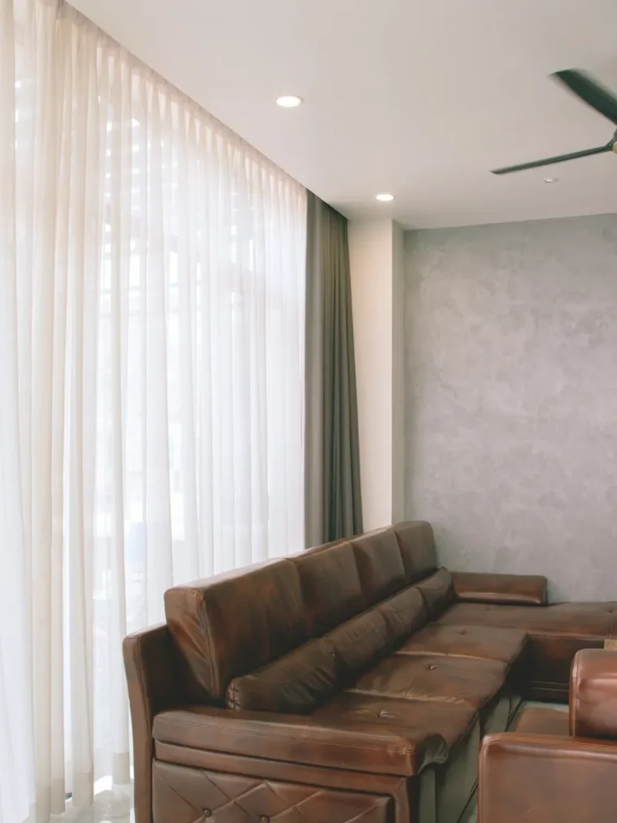 Floor-to-ceiling sheer curtains on a ceiling track beside a leather sofa and ceiling fan