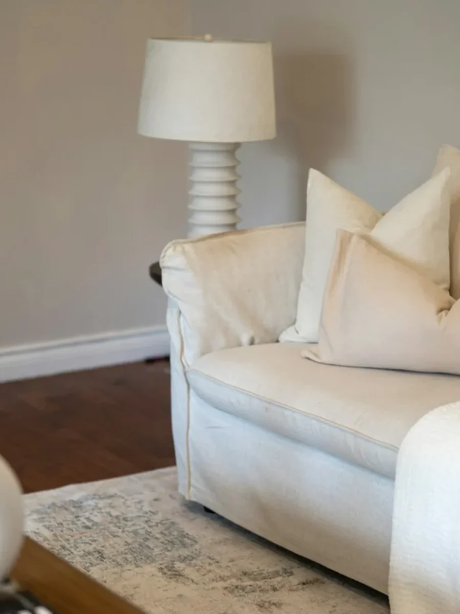 Cream slipcovered sofa with matching cushions and a knitted throw beside a white table lamp