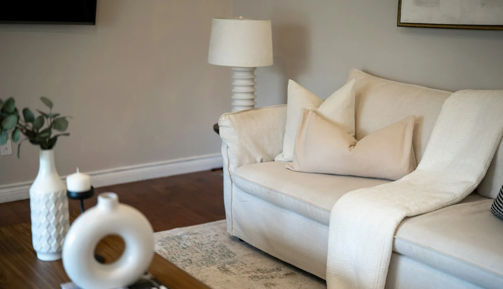 Cream slipcovered sofa with matching cushions and a knitted throw beside a white table lamp