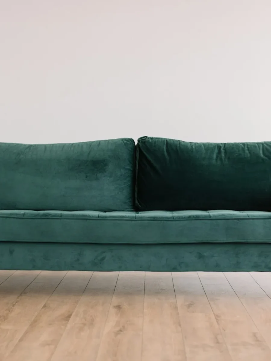 Green velvet three-seater sofa raised on tapered wooden legs on a pale wood floor