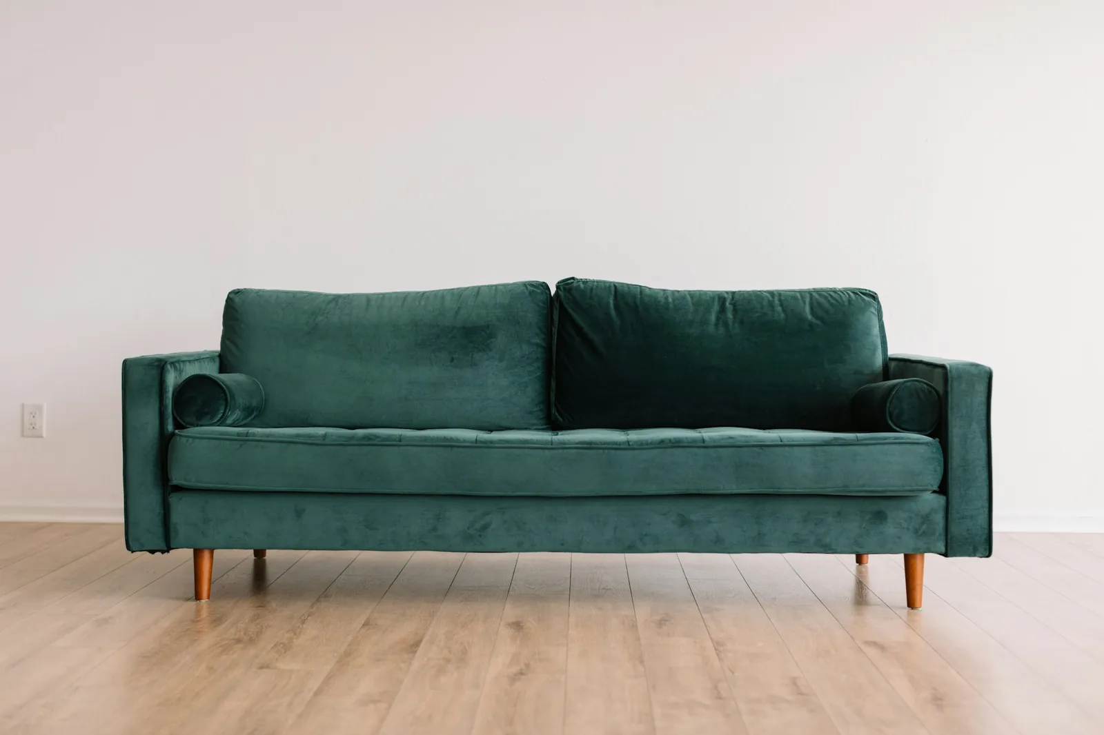Green velvet three-seater sofa raised on tapered wooden legs on a pale wood floor
