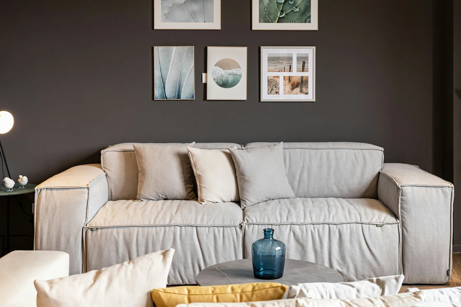 Loose-covered grey fabric sofa with cushions against a dark charcoal wall
