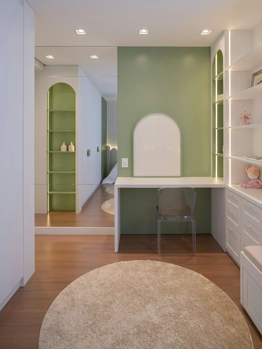 A study nook with a built-in white desk, sage-green wall, arched shelves and a round rug