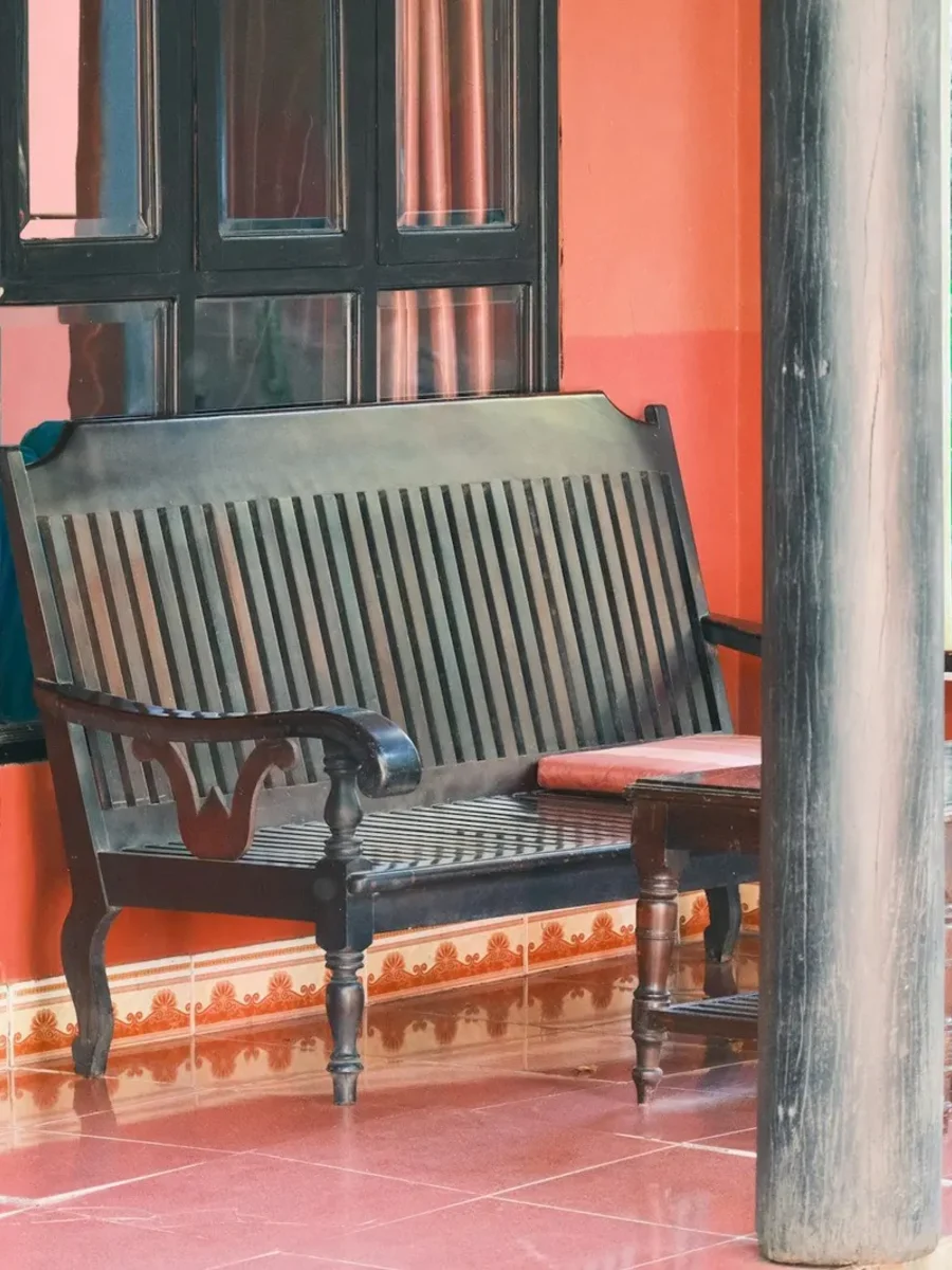 Dark wooden bench and table on a red-tiled verandah between timber pillars and greenery