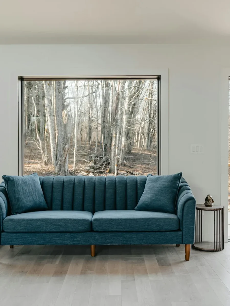 Teal three-seater sofa on wooden legs between two large picture windows and an open door