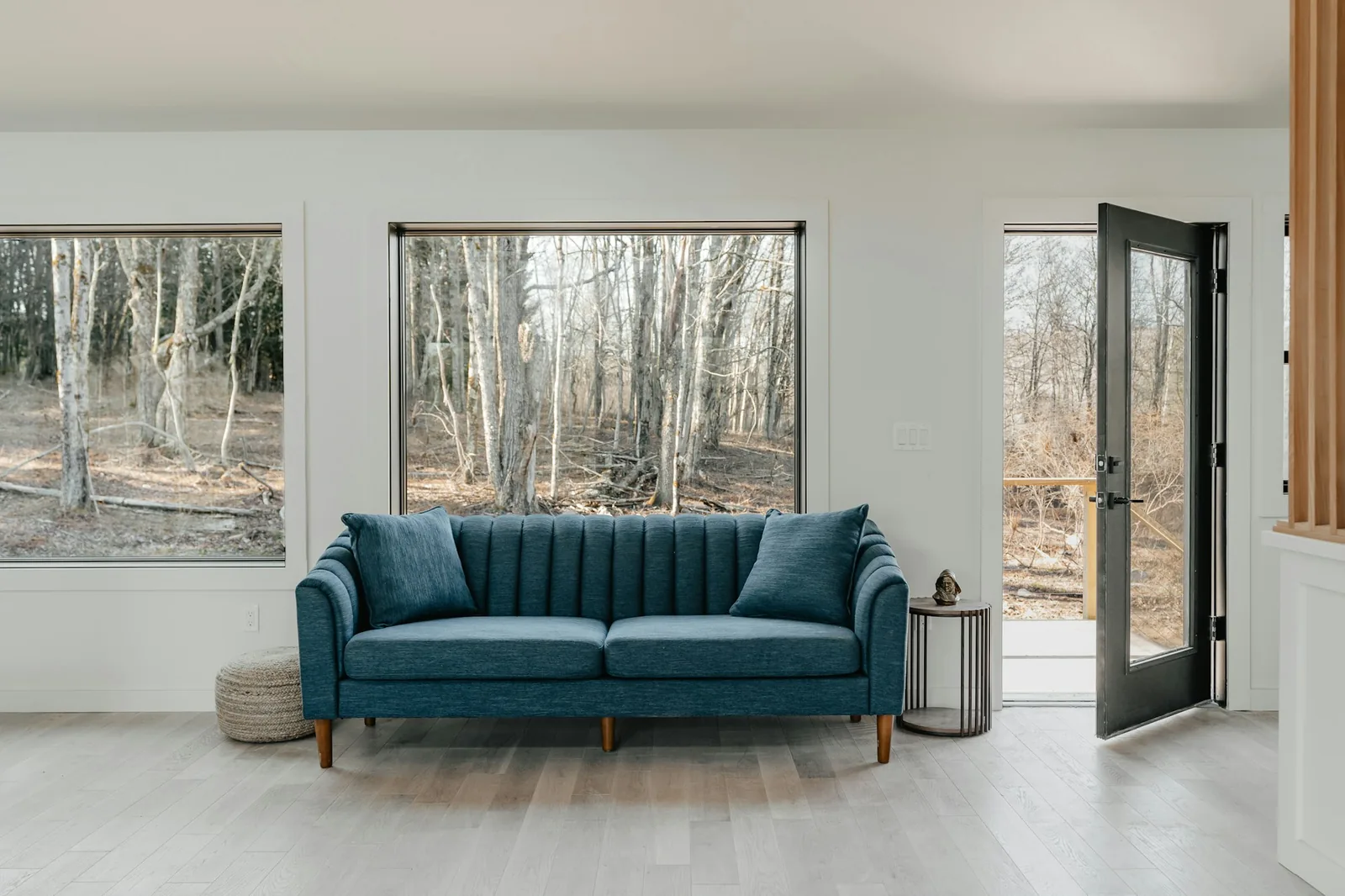 Teal three-seater sofa on wooden legs between two large picture windows and an open door