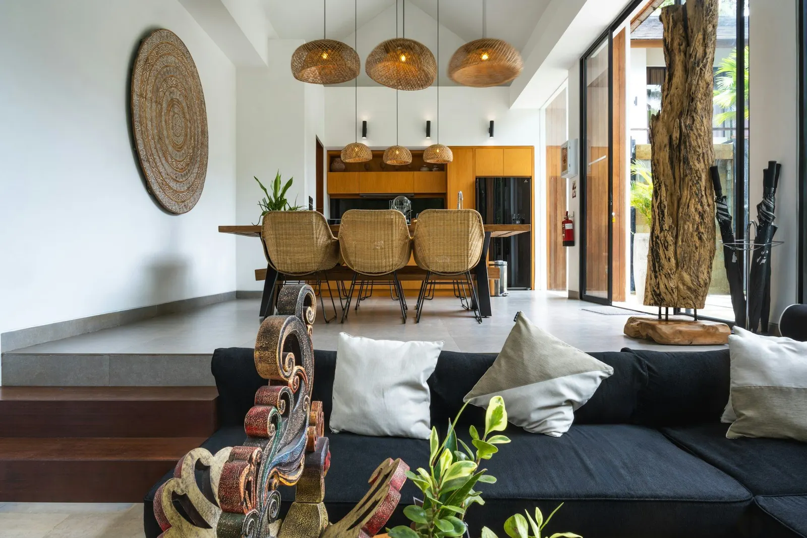 Open-plan living and dining space with rattan chairs, woven pendant lights and plants