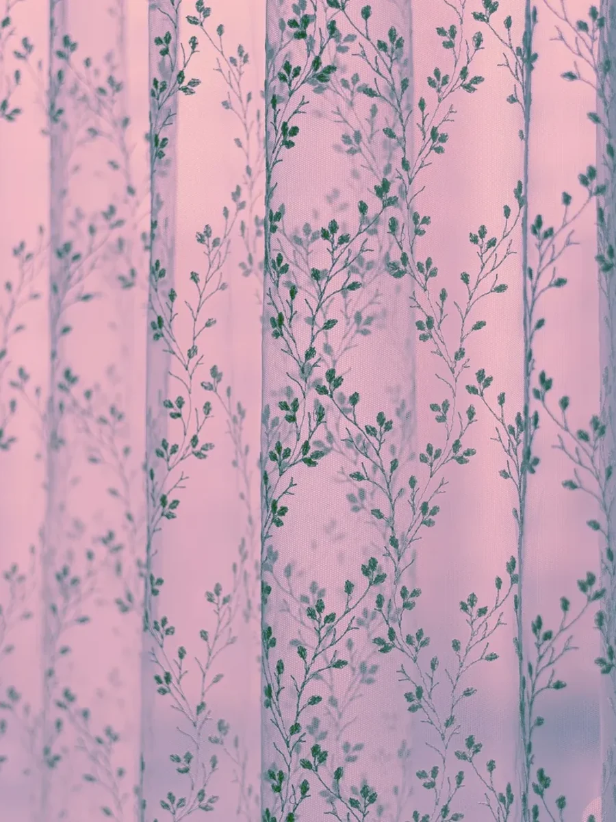 A sheer voile printed with climbing leaves layered beside a solid green curtain panel