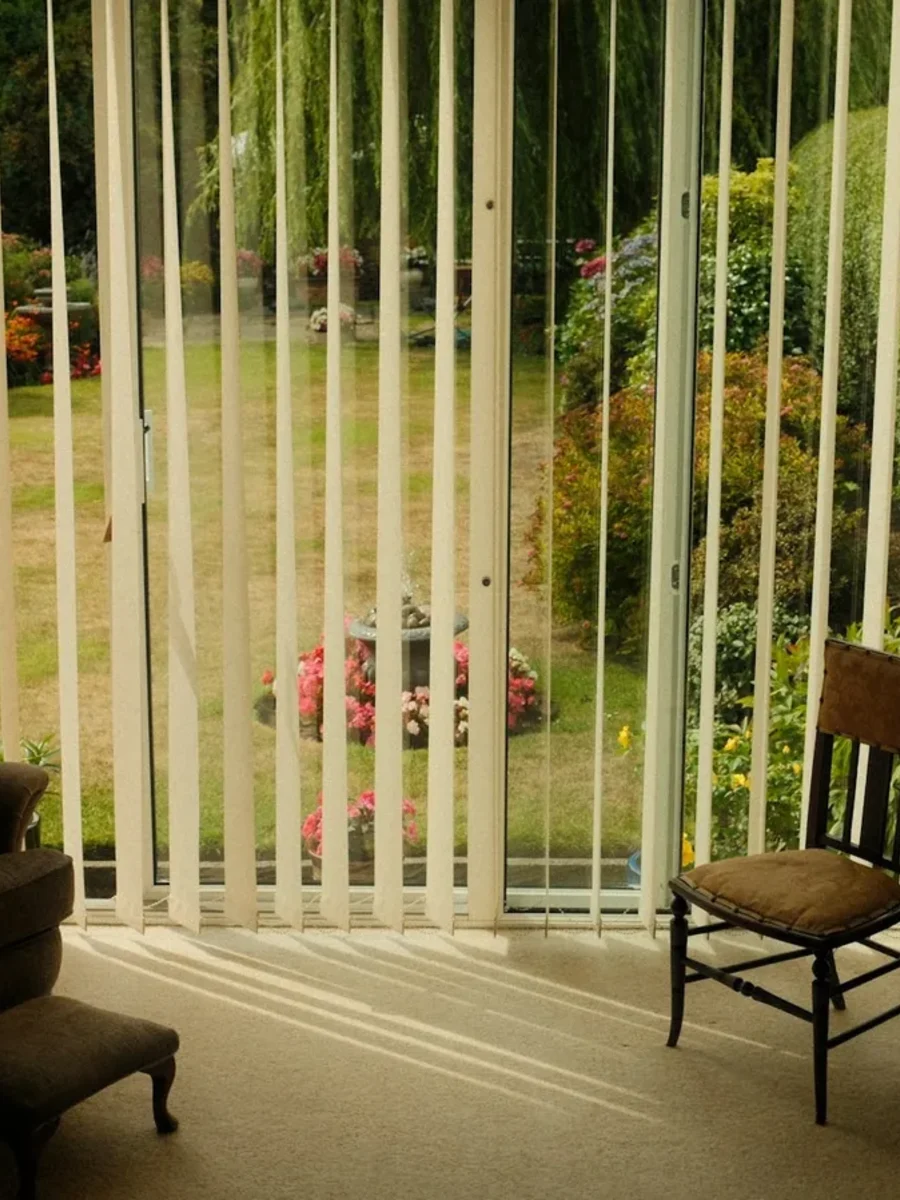 Cream vertical blinds drawn back from a wide garden door in a traditionally furnished sitting room