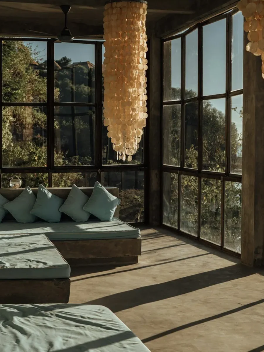 Living room wrapped in tall black-framed windows, with sea-green sofas and capiz shell chandeliers