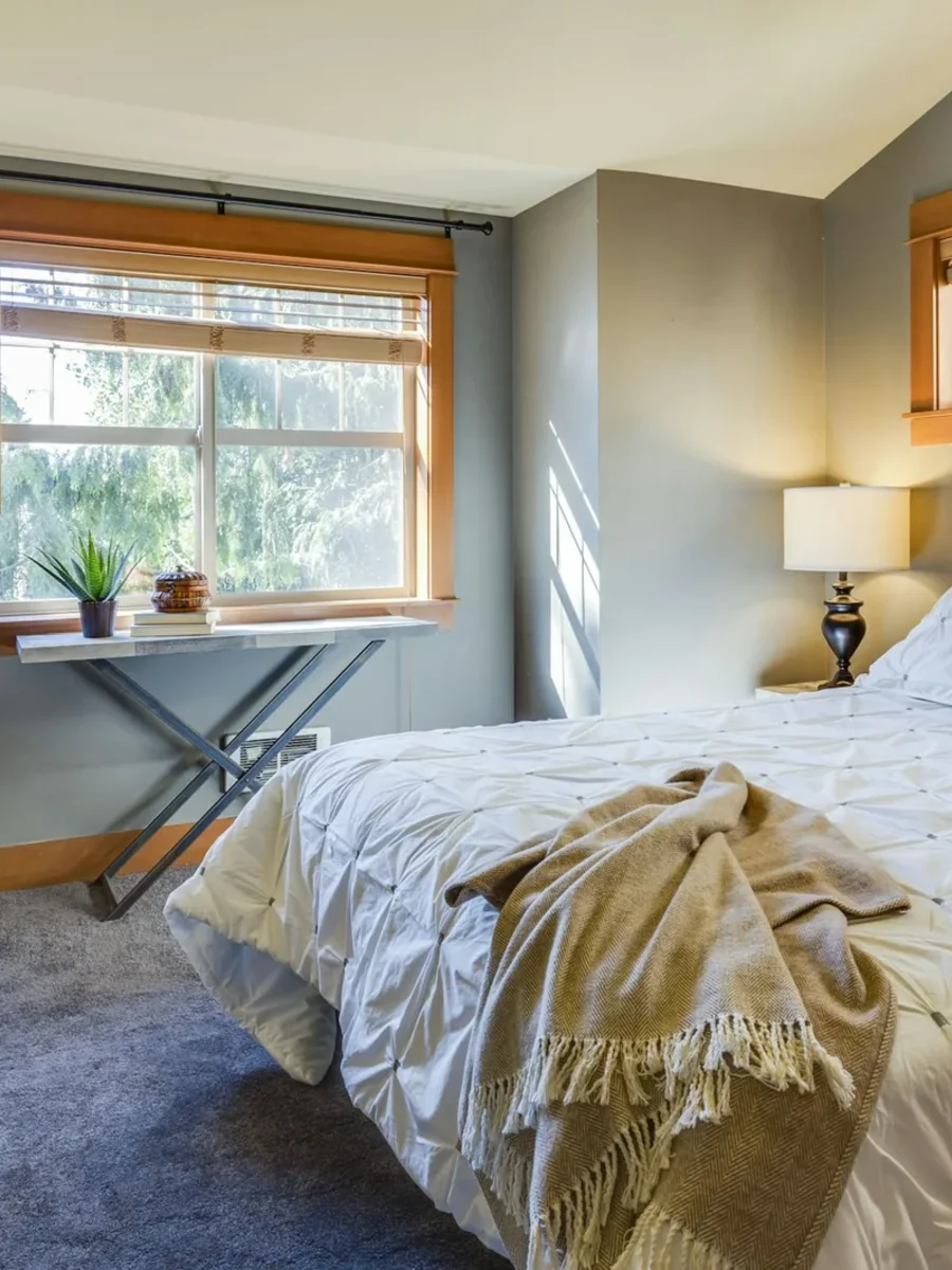 Bedroom with grey wall-to-wall carpet, timber-framed windows and a white quilted bed