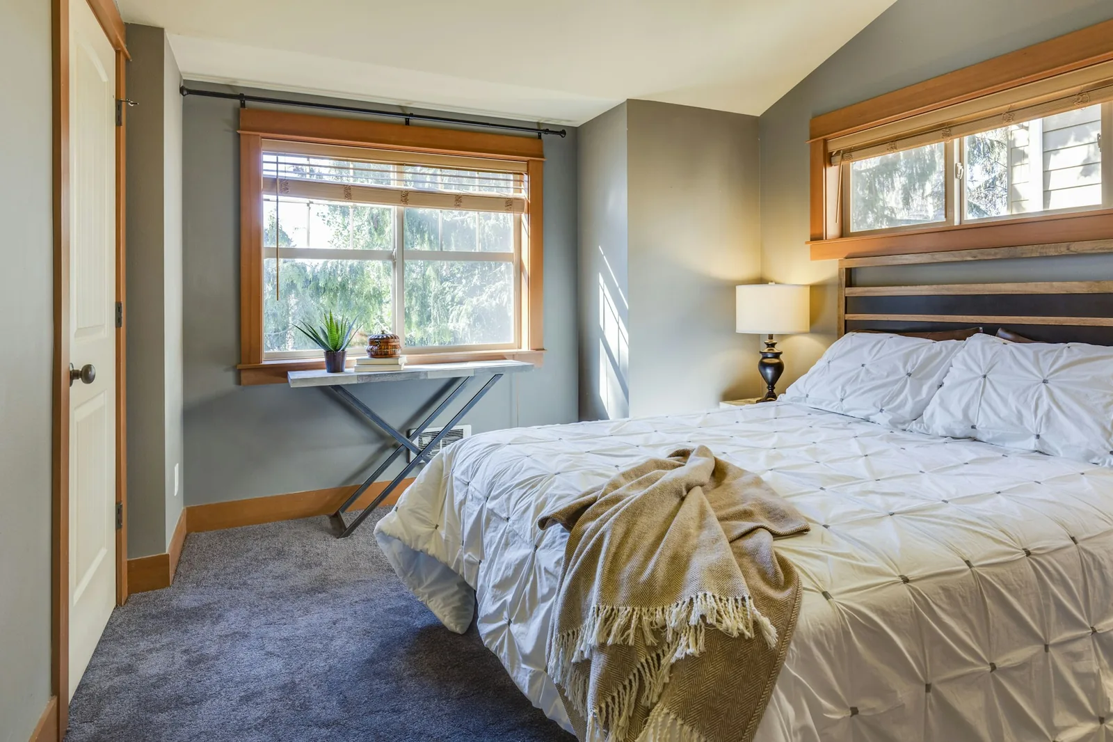 Bedroom with grey wall-to-wall carpet, timber-framed windows and a white quilted bed