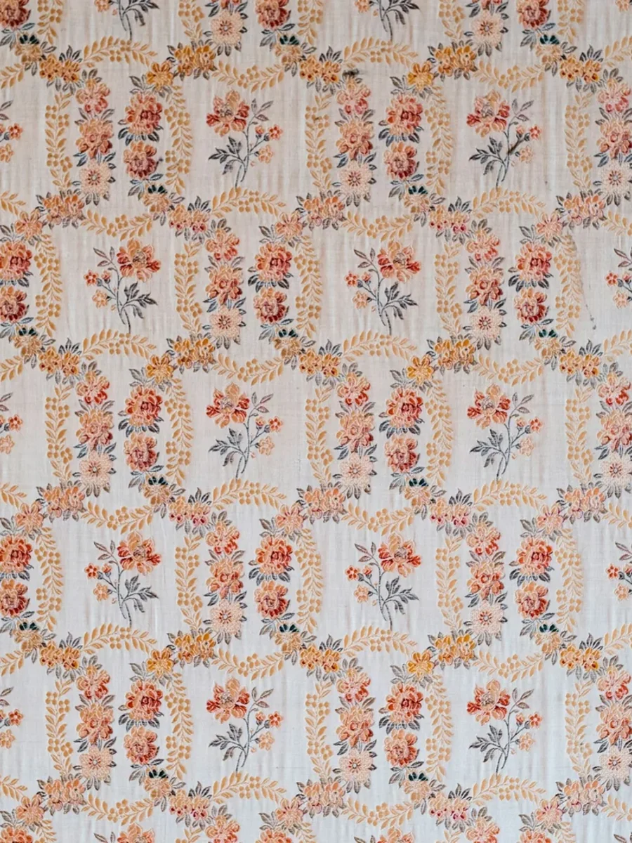 A wall covered in repeating floral wallpaper, sprigs of orange roses on a pale blue ground