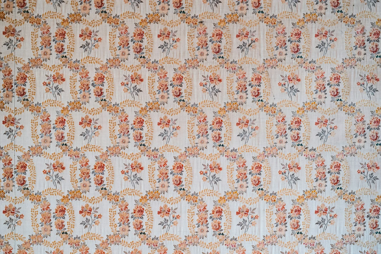 A wall covered in repeating floral wallpaper, sprigs of orange roses on a pale blue ground