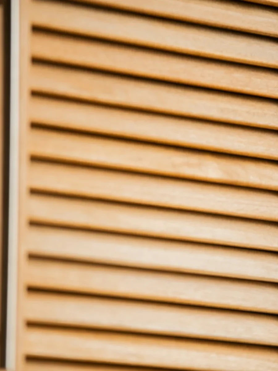 Close view of a light wooden louvred cupboard door with angled slats and hinges
