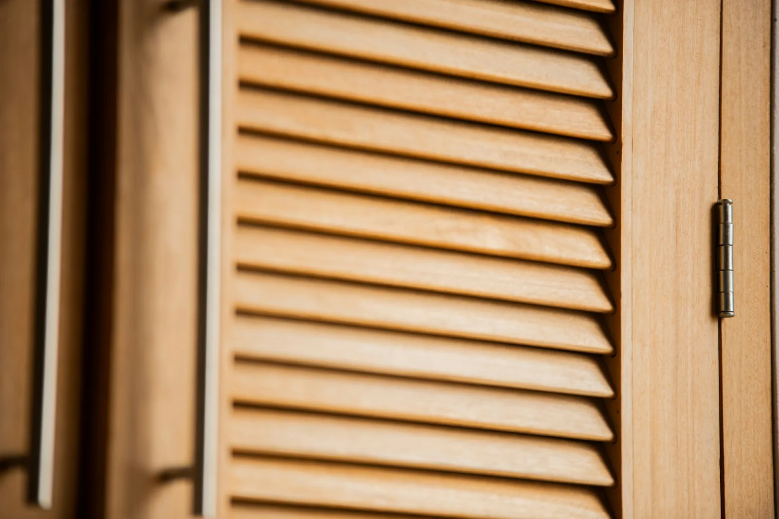 Close view of a light wooden louvred cupboard door with angled slats and hinges