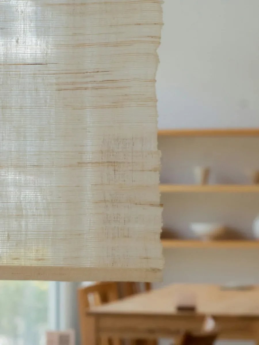 Close view of a raw-linen fabric blind lowered at a window, wooden shelves blurred behind