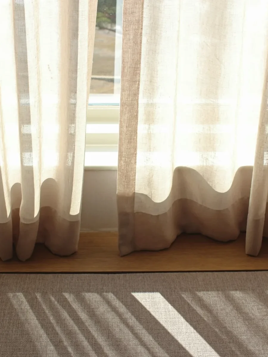 Sheer linen curtains falling in soft even ripples onto a window sill in morning sun