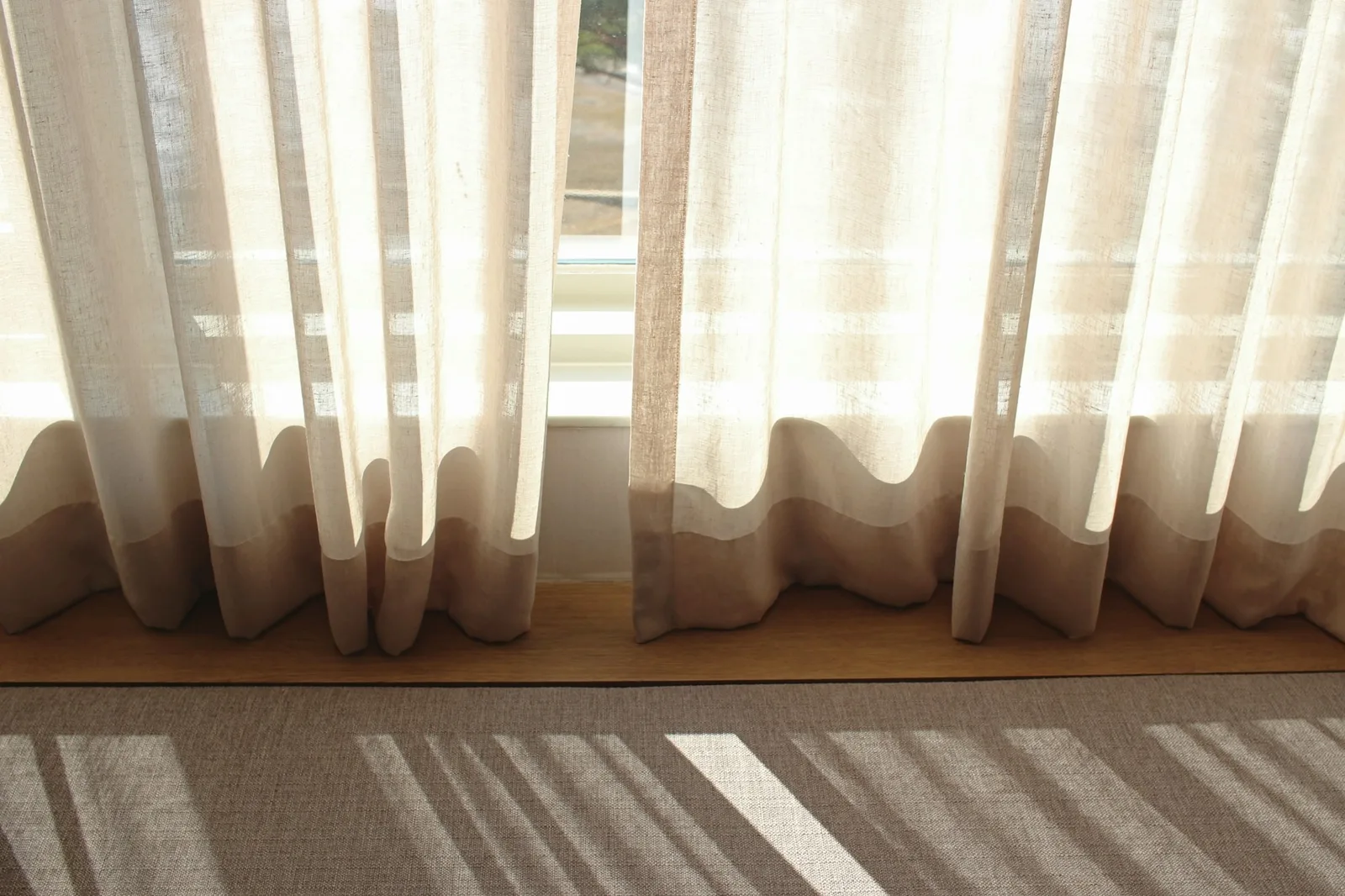 Sheer linen curtains falling in soft even ripples onto a window sill in morning sun