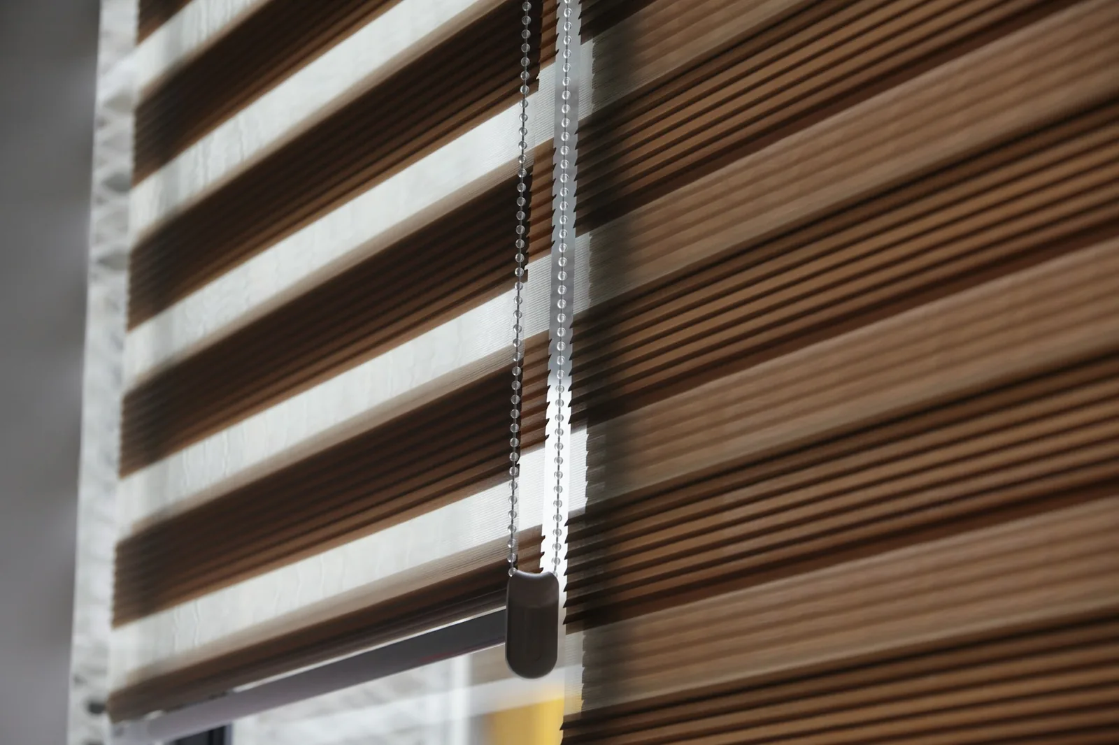 Brown and sheer striped zebra blind with a beaded chain control at a window