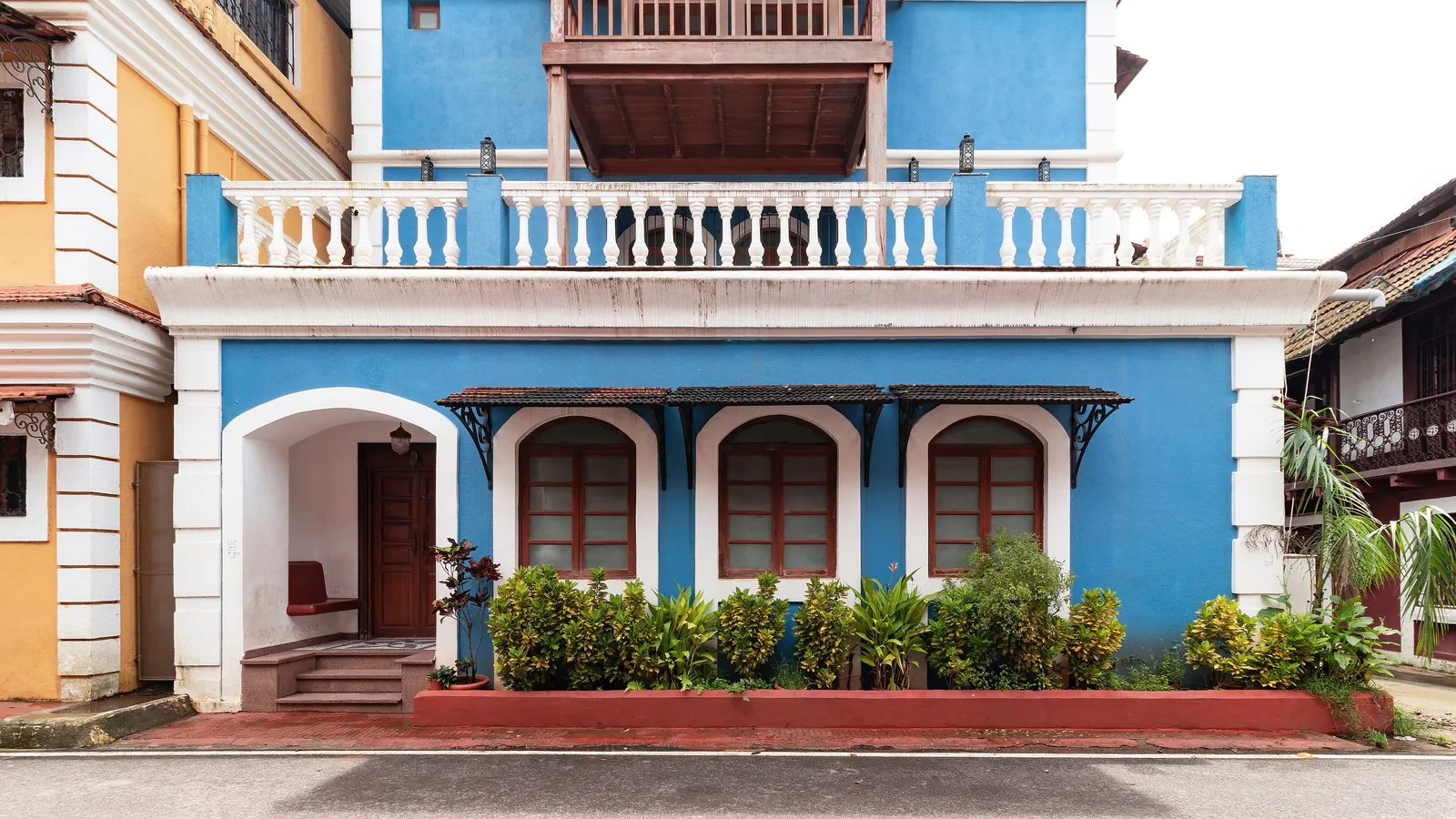 A bright blue Fontainhas house in Panaji with white balustrade, arched windows and a yellow neighbour