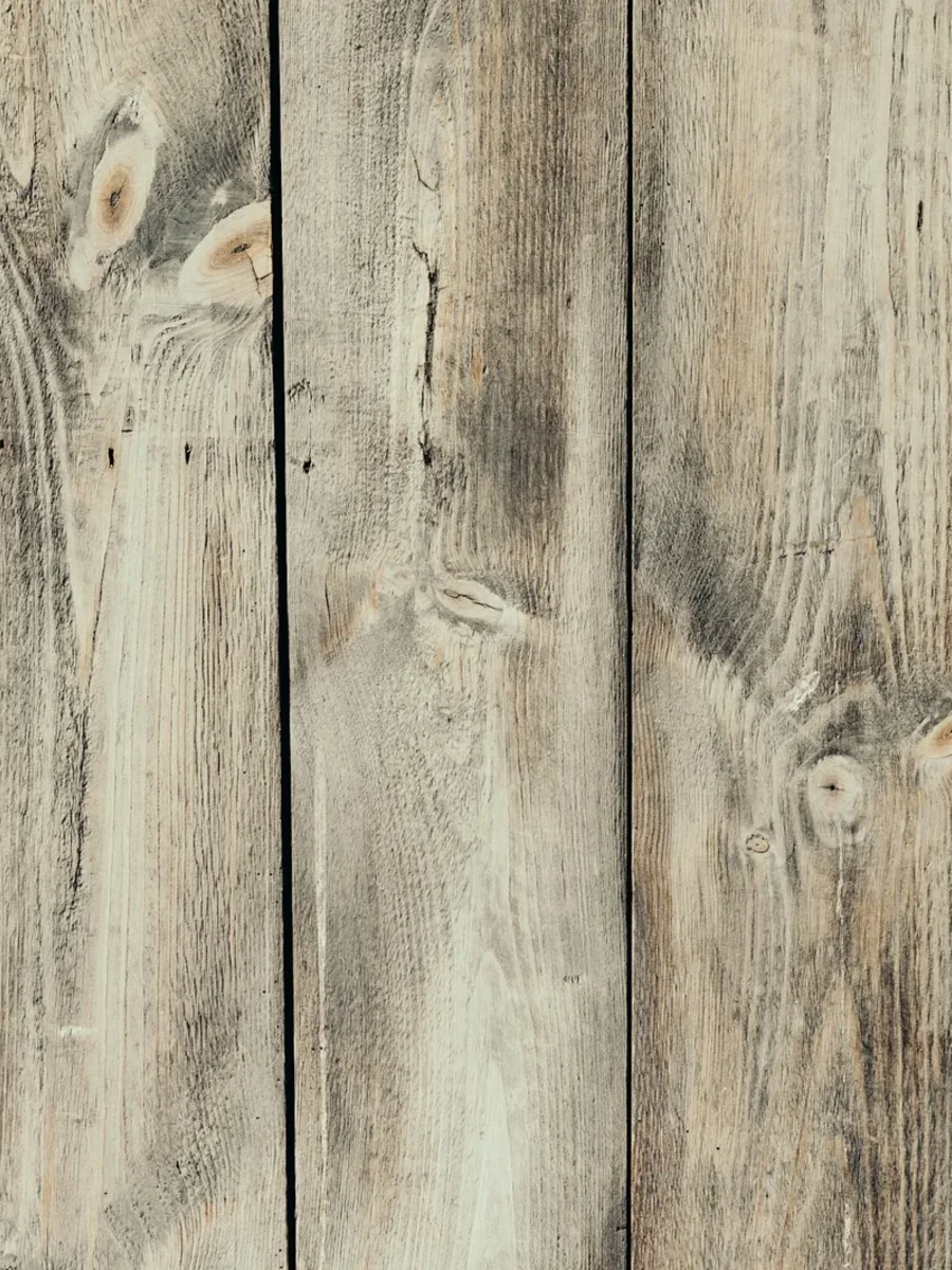 Weathered pale timber planks laid vertically, with knots and grain clearly visible across the boards