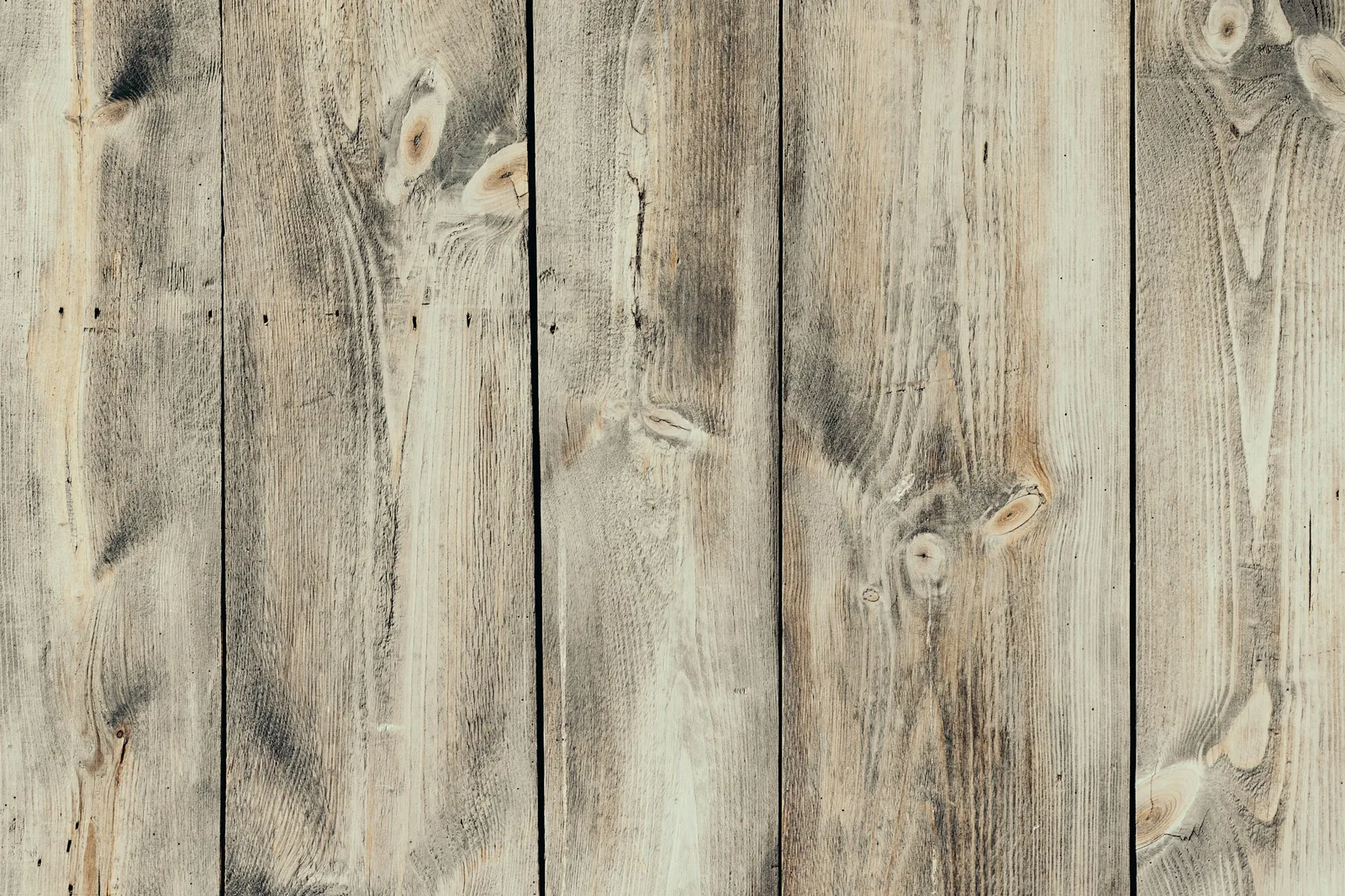 Weathered pale timber planks laid vertically, with knots and grain clearly visible across the boards