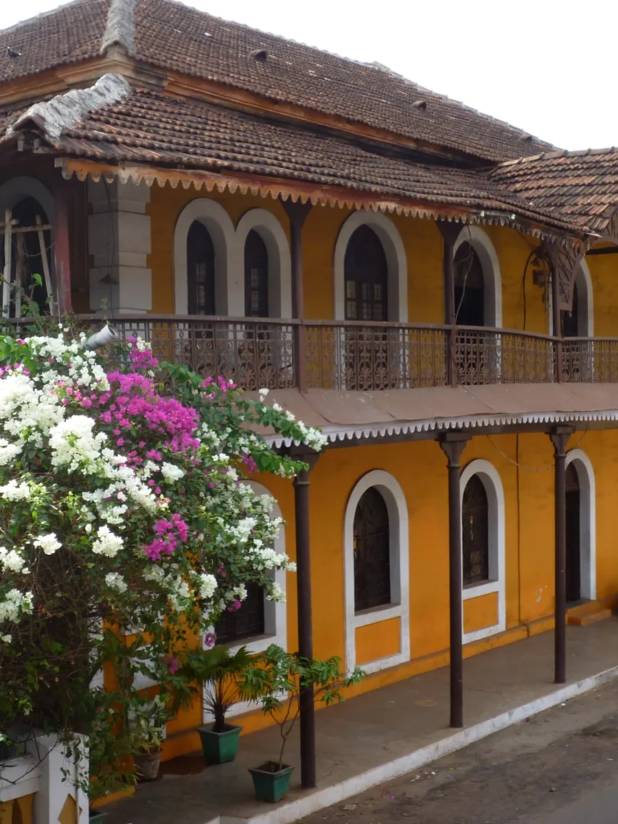 Ochre-yellow two-storey house in Fontainhas, Panjim, with a long iron balcony and bougainvillea in flower