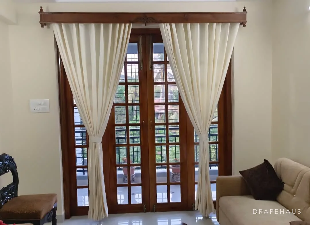 Ivory sheer curtains tied back on a carved hardwood pelmet above timber French doors in a traditional Goan house