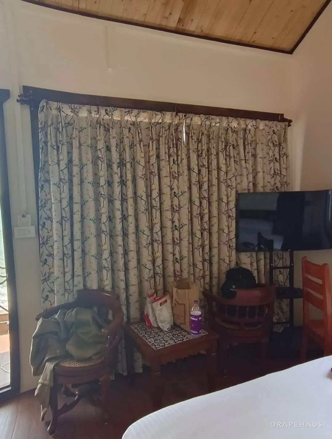 Printed botanical curtains on a timber pole in a resort guest room with a pitched timber ceiling