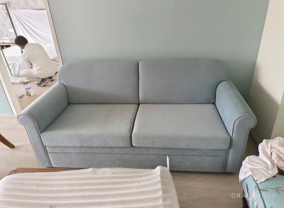 Sofa reupholstered in sage green fabric with contrast piping, photographed during a renovation