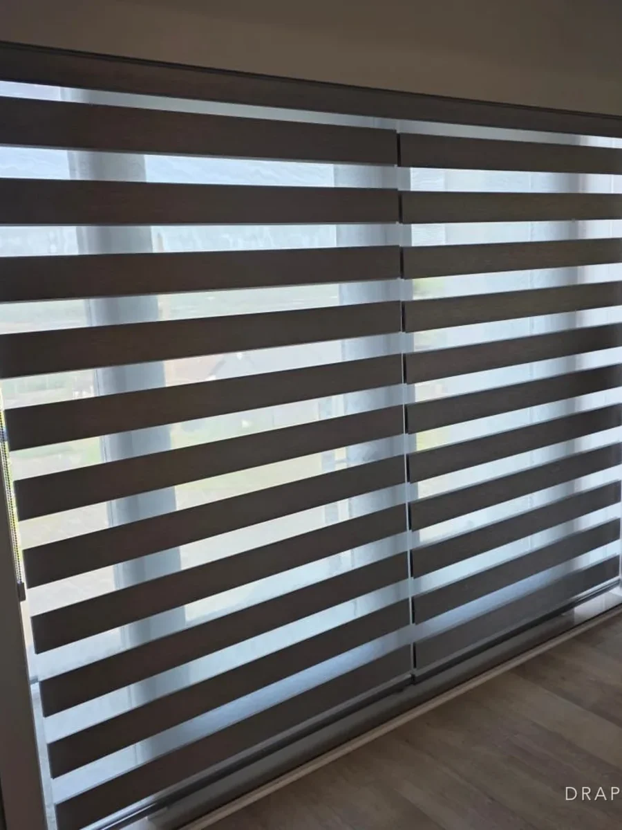 Zebra blinds across a wide opening, the bands part-aligned to let light through