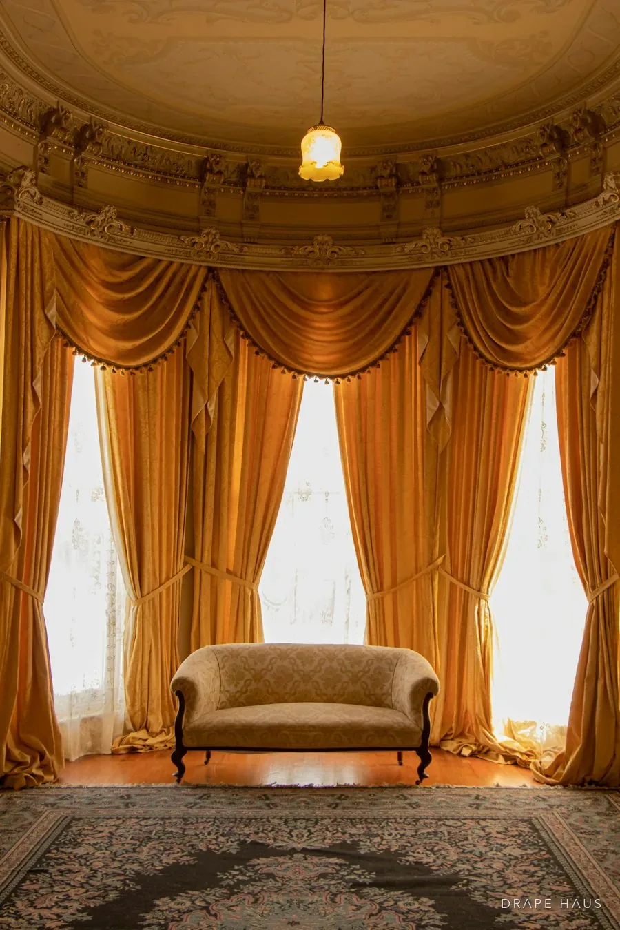 Full-height gold curtains framing tall windows in a high-ceilinged heritage room