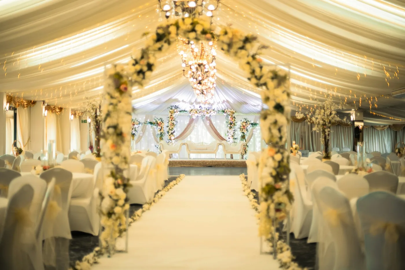 A banquet hall set for an event, with draped walls and a fabric backdrop behind the stage