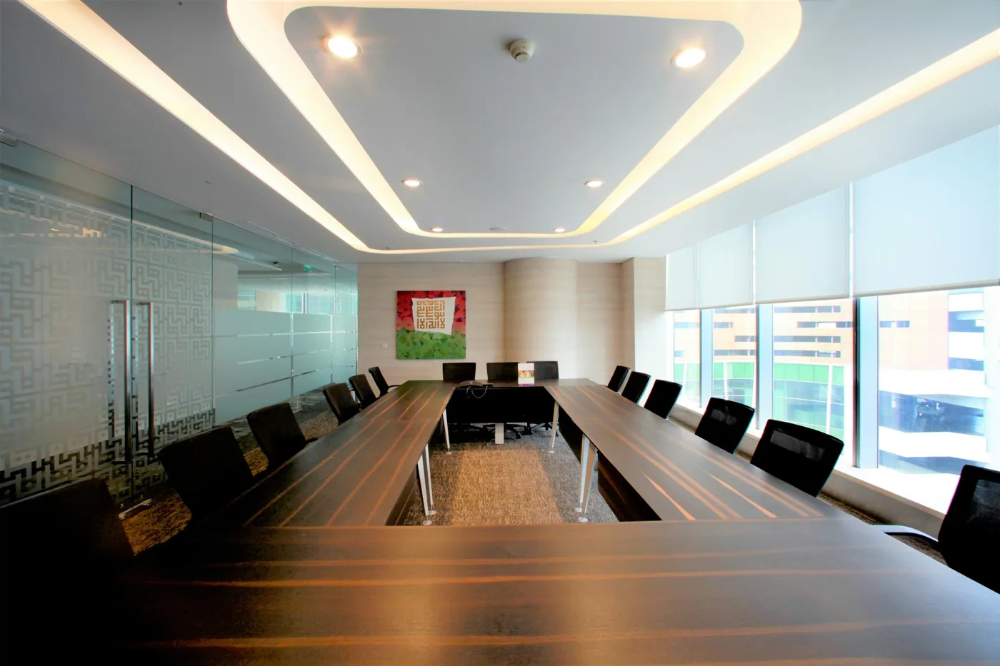 A conference room with a long table, a wall-mounted screen and shaded windows