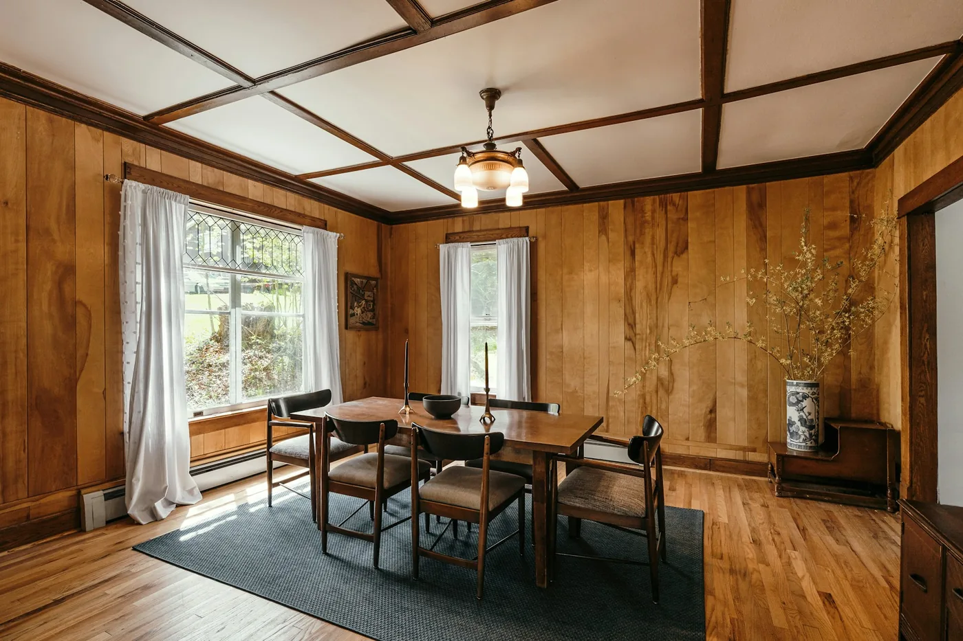 A dining table with chairs beside a window dressed with light curtains in a Goan home