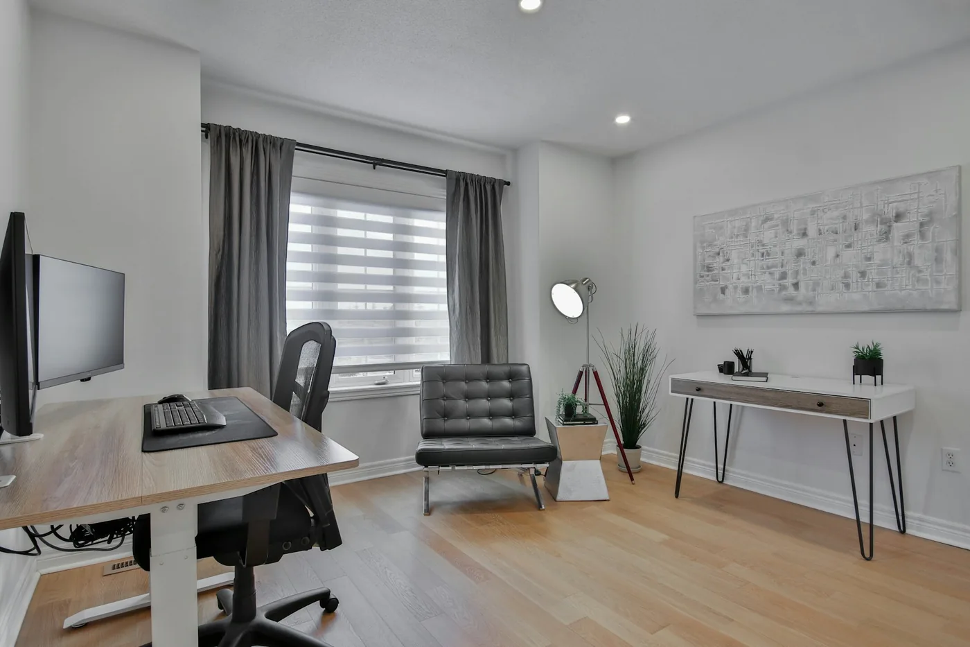 A home office desk beside a window with a blind and a calm wall behind the chair